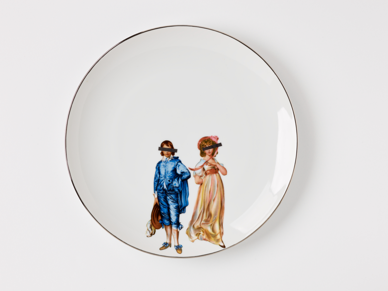 White circular plate with silver rim. Two figures at the lower center of the plate, one dressed in a blue outfit, the other in a pink dress, both with black, rectangular bars covering their eyes.