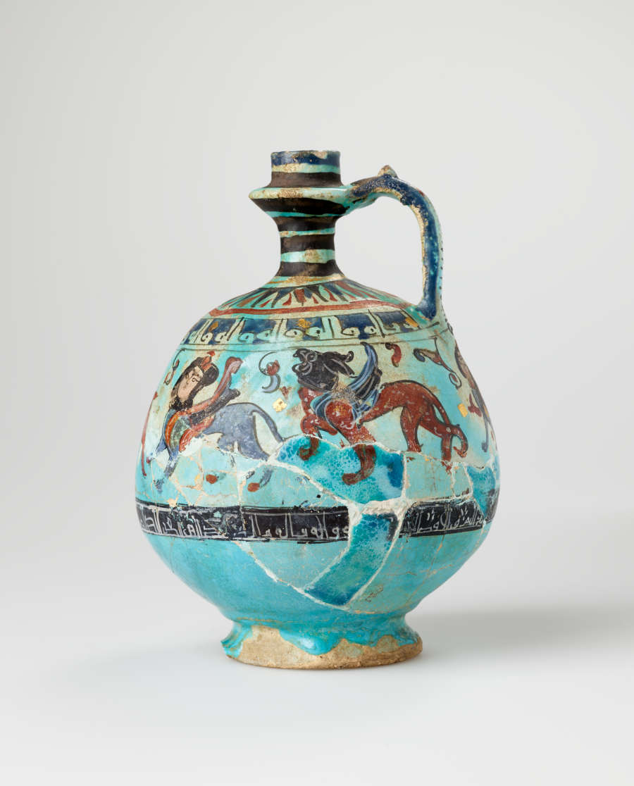 The same blue spherical jug with a slender neck and a handle, decorated with illustrations of humanoid creatures and patterns, turned slightly. It shows signs of wear, breakage, and repair.