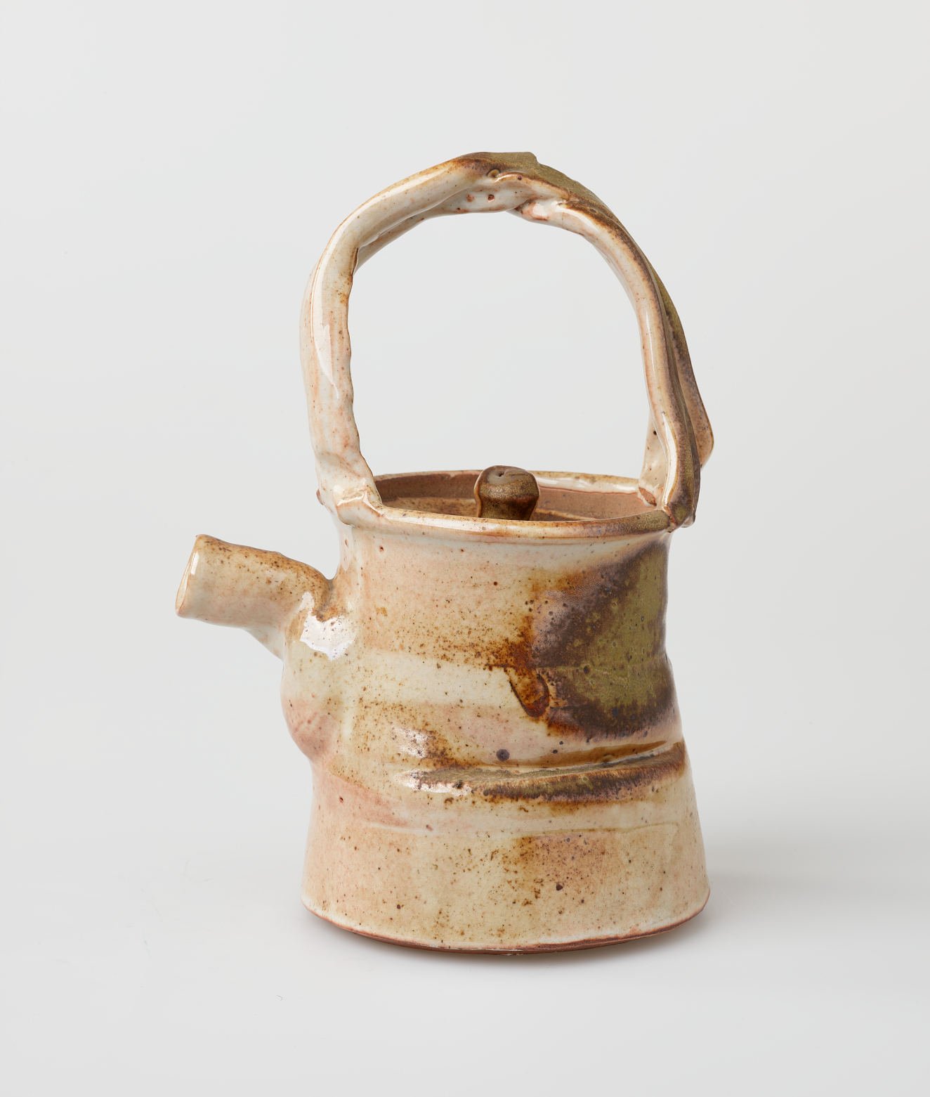 Ceramic teapot with an arched handle, flared base, short spout, and sunken lid. A glossy cream glaze and horizontal bands and patches of reddish-brown covers the body.