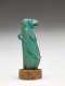 Side-view of the aquamarine sculpture of a nude anthropomorphic hippo-headed woman with bare breasts, long hair and arms, and sculpted loop on its back. It’s mounted on a stone disk.