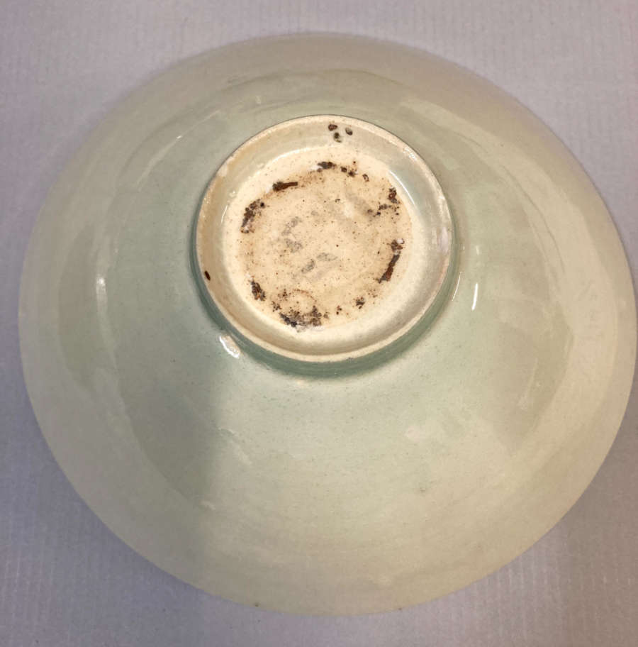 Bottom view of a glossy pale and green-gray bowl on a gray textured background. Its small circular base protrudes inwards and is white with brown stains. 