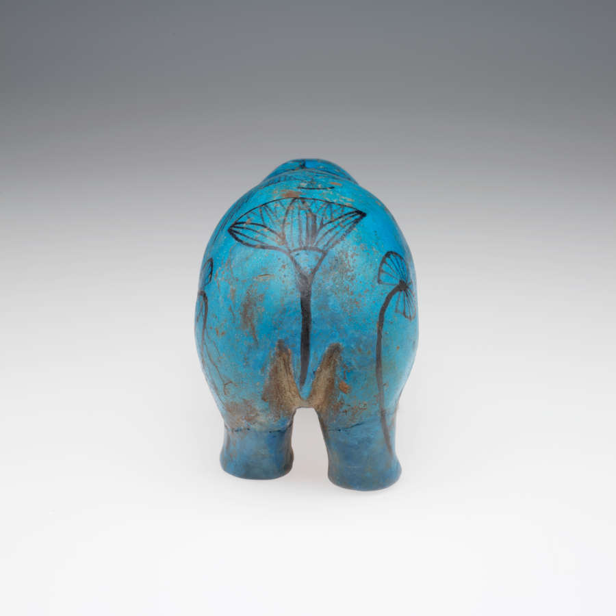 A back view of a blue sculpture of a standing hippopotamus with black outlines of birds, insects, plants and waves on its glossy surface. 