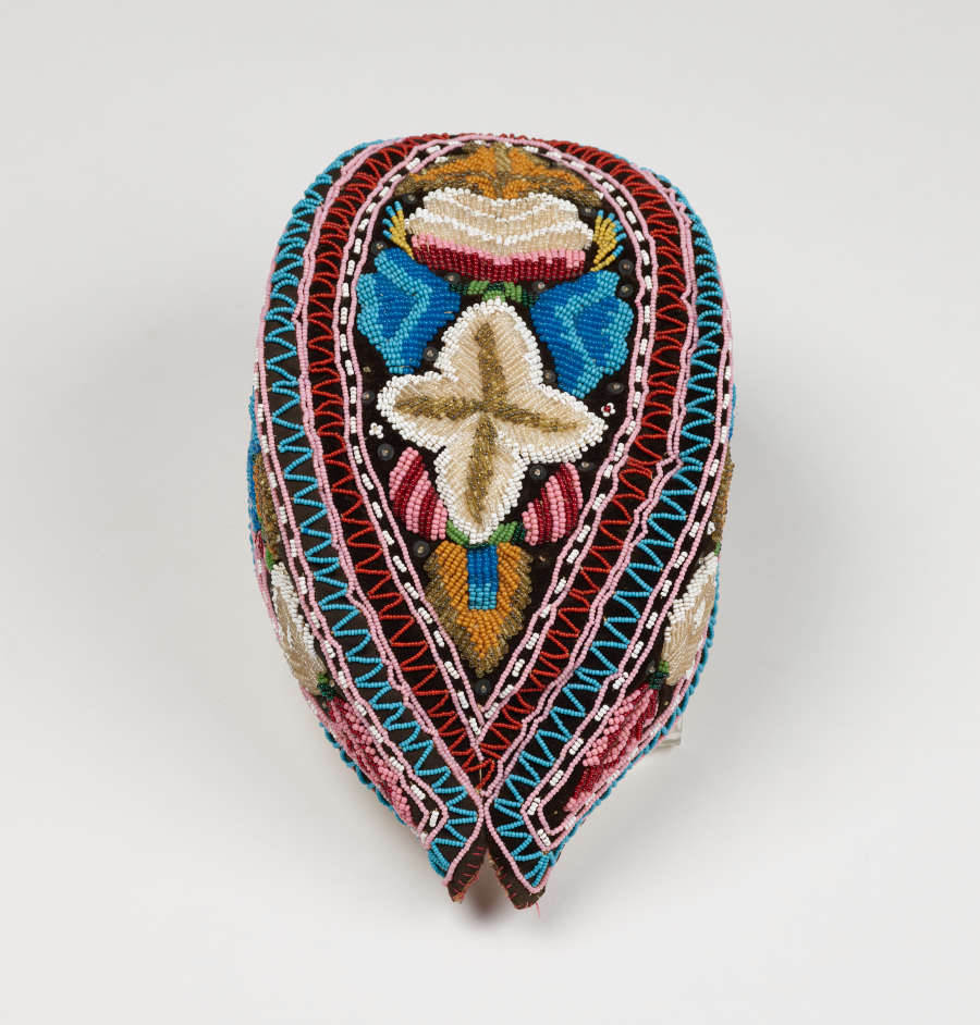 Top view of an almond shape cap, which features 3 blocks of intricate floral embroidery in whites, ochres, blues and pinks, framed by colorful patterns. The top face is teardrop-shaped.