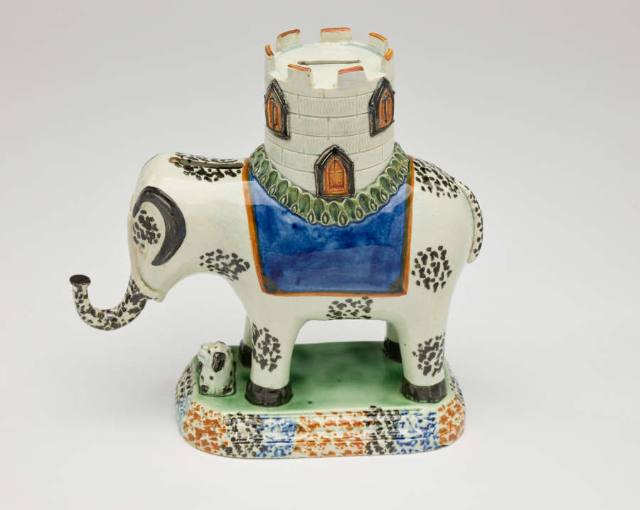  A sculpture in the shape of an elephant with a castle on its back. The decorations are white, blue, green, and yellow.
