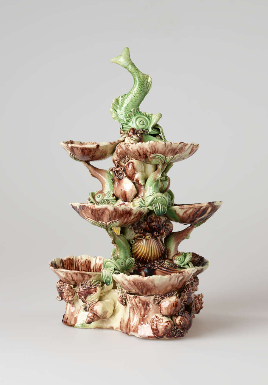 An elaborate, sculptural, three-tiered dish. Colored in brown, green, and cream with floral decorations as well as sculpted fish decorations.