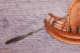 A close-up of a painted scene on a ceramic bowl depicting a small wooden boat with a woven canopy, a single oar extending off the side into purple-hued water.