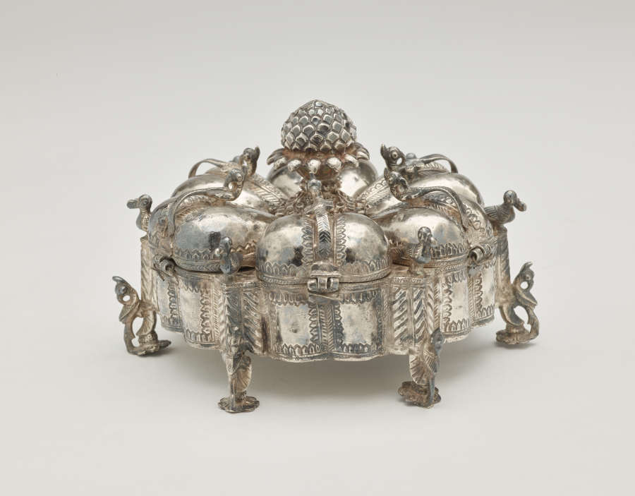 A dark silver spice box that is sculptural and has many different rounded compartments.
