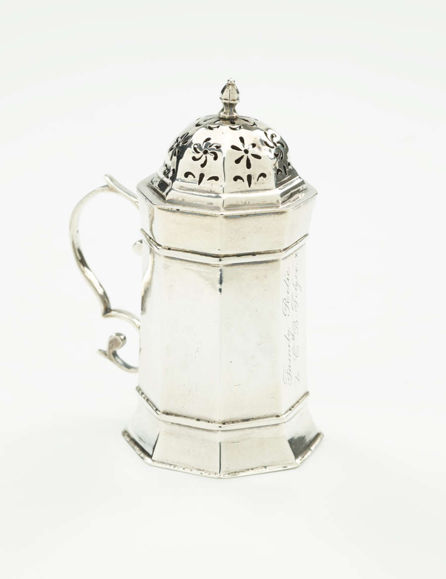  A silver vessel that has an octagonal body, handle, and lid that has floral perforations.
