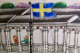 A close up of a painted ceramic showing figures along a building facade with arched windows and ornate barriers and a Swedish flag flying on a pole in the foreground.