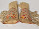 A pair of tan gloves, each with fringed and patterned beaded edges and embroidered with a colorful floral pattern on the cuffs, viewed so that its suede interior is visible.