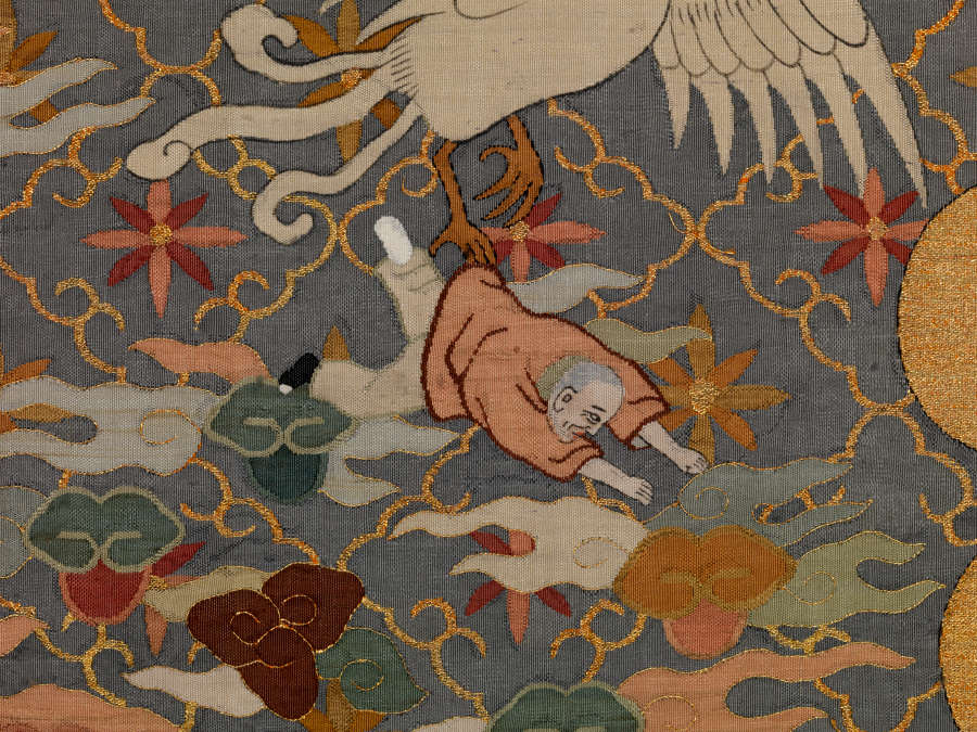 Robe’s back detail, showing a monk flailing on the ground, amongst earthy pastel clouds, a flying white bird, against a dark background with a diagonally running grid and floral motifs.