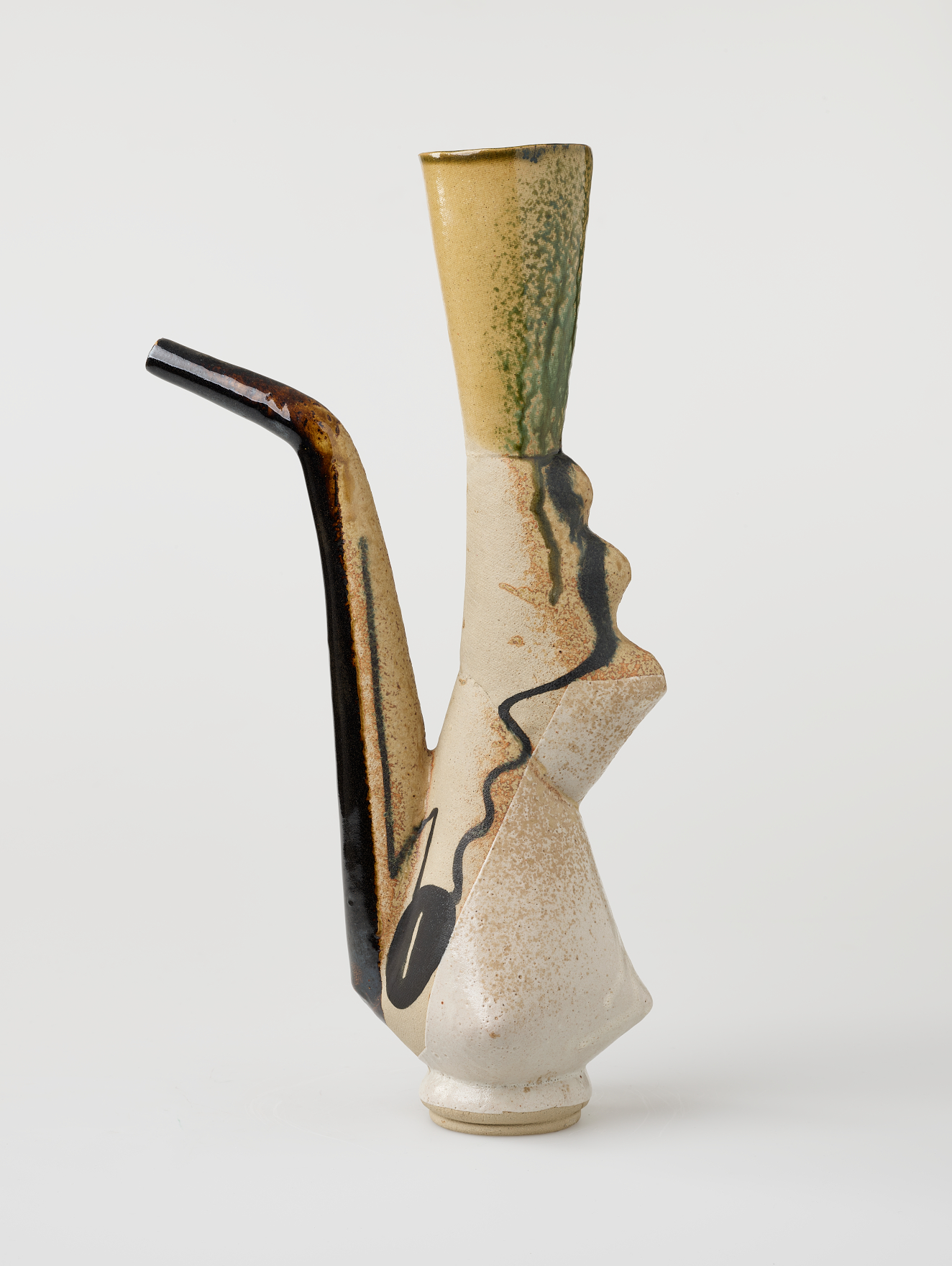 Tall, angular vessel with a flared green-speckled neck and a black spout bent at an angle. The cream-glazed body is matte and decorated with bold black lines. 