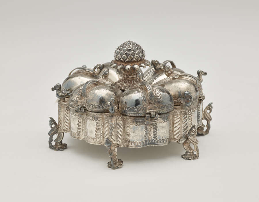 A dark silver spice box that is sculptural and has many different rounded compartments.
