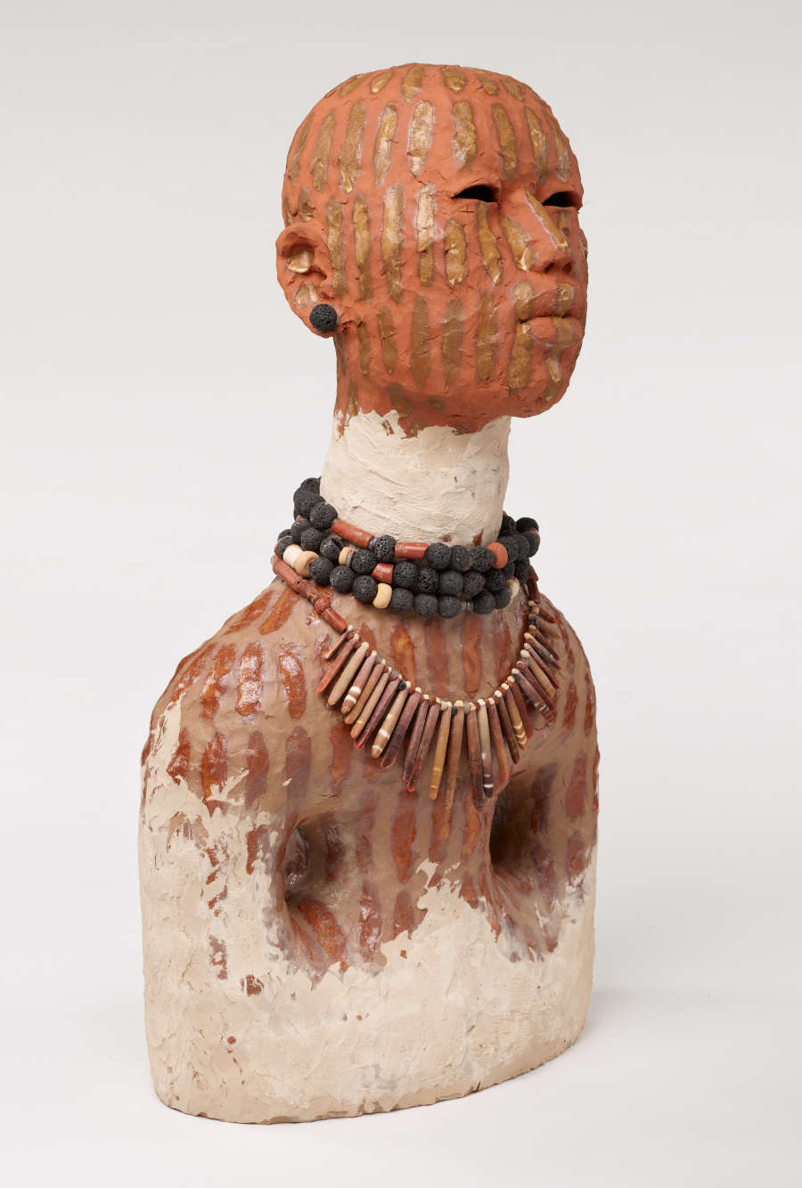Side view of the same bust. Their neck is painted white and a white silhouette forming two breasts is painted on the bottom of their torso. The figure looks straight ahead. 