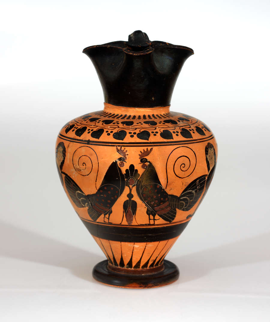 Black and orange onion-shaped jar with the pinched mouth facing the viewer. Visible are illustrations of two roosters facing one-another next to those of the sphinx.