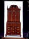 A tall standing cabinet made of polished mahogany wood with intricate metal handles on the lower drawers, fan-shaped carvings on the upper panels, and a rounded top featuring a curving inset.