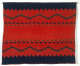 Red woven tapestry with blue-black geometric triangles and zigzag patterns. The tapestry has a blue-black jagged trim and the patterns are horizontally mirrored along the center.