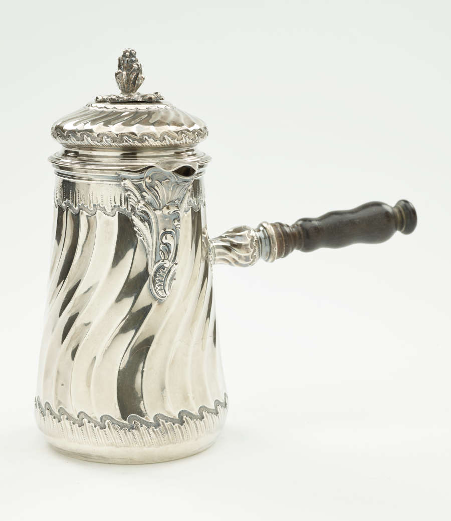 A silver chocolate pot with a decorative swirled body, lid, and fruit wood handle.