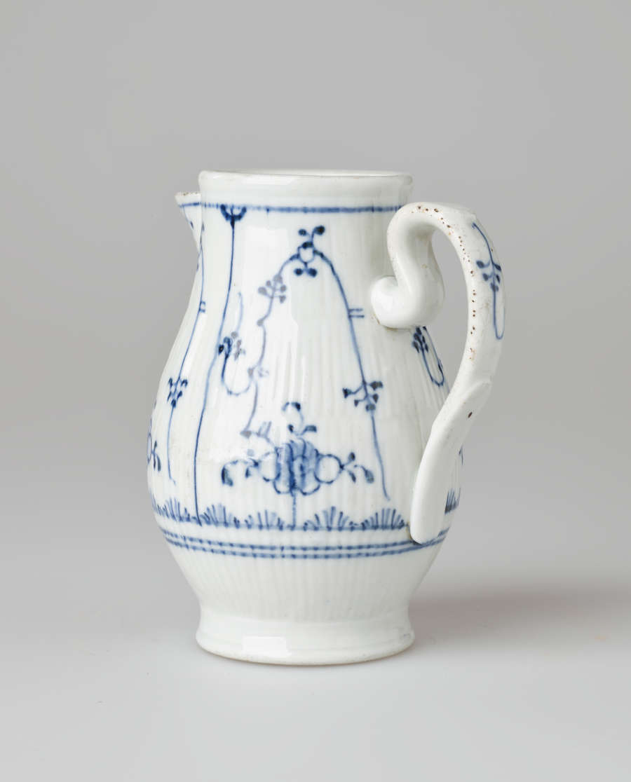 A white chocolate pot with delicate blue decorations with ribbed body, spout, handle, and foot.