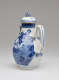 A white and blue chocolate pot with a spout, handle, and lid, the edges of the lid and spout are gilded. The decorations mainly depict floral, architectural, and landscape elements.