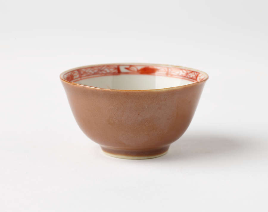 A small ceramic bowl with a smooth brown exterior, and a red geometric border on the interior