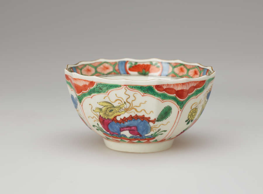 A white bowl with green, red, blue, pink, yellow and gilded decorations. The lip of the vessel is scalloped.