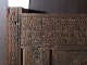 A close up of an intricately carved wooden corner featuring geometric and floral motifs, with signs of wear and damage along the left edge. 
