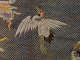 An embroidered white crane with orange and black details, outstretched wings, and long slender legs, surrounded by swirling clouds on a gold lattice background.