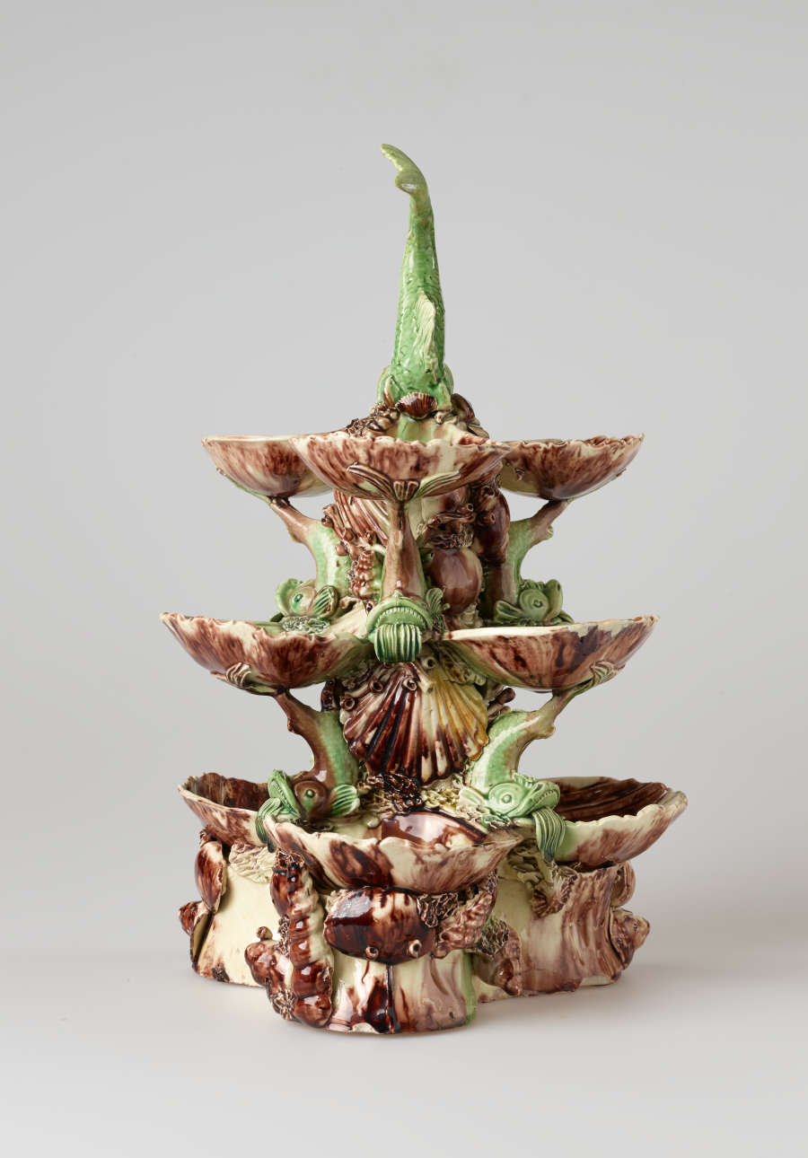 An elaborate, sculptural, three-tiered dish. Colored in brown, green, and cream with floral decorations as well as sculpted fish decorations.