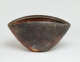 Back of a clam-shaped stone bowl with a slightly protruding rim and shell-like etchings on its brown, speckled exterior and a red-orange interior. Near its base is a white-orange blemish.