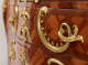 A close-up image of intricately swirled golden handles on an ornate wooden dresser with a warm, glossy finish.