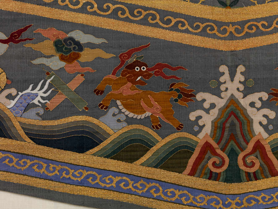 Border of the triangular tail of the gray-blue robe’s back, featuring an animal leaping away from an erupting wave, with earthy-pastel clouds. It is framed by a golden border.
