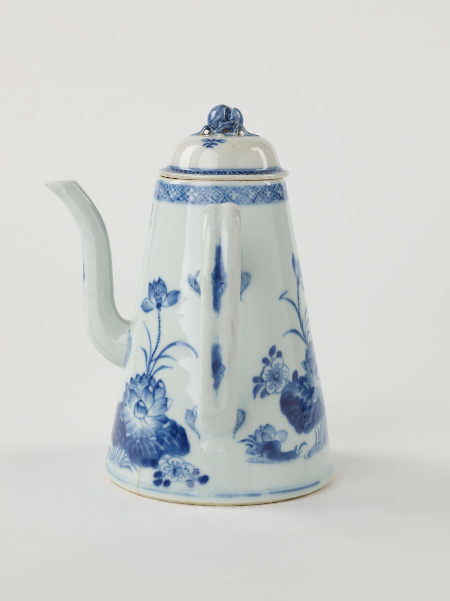 A white and blue teapot with floral decorations, a lid with a small semi spherical finial, spout, and a handle which is located approximately 90 degrees from the spout.