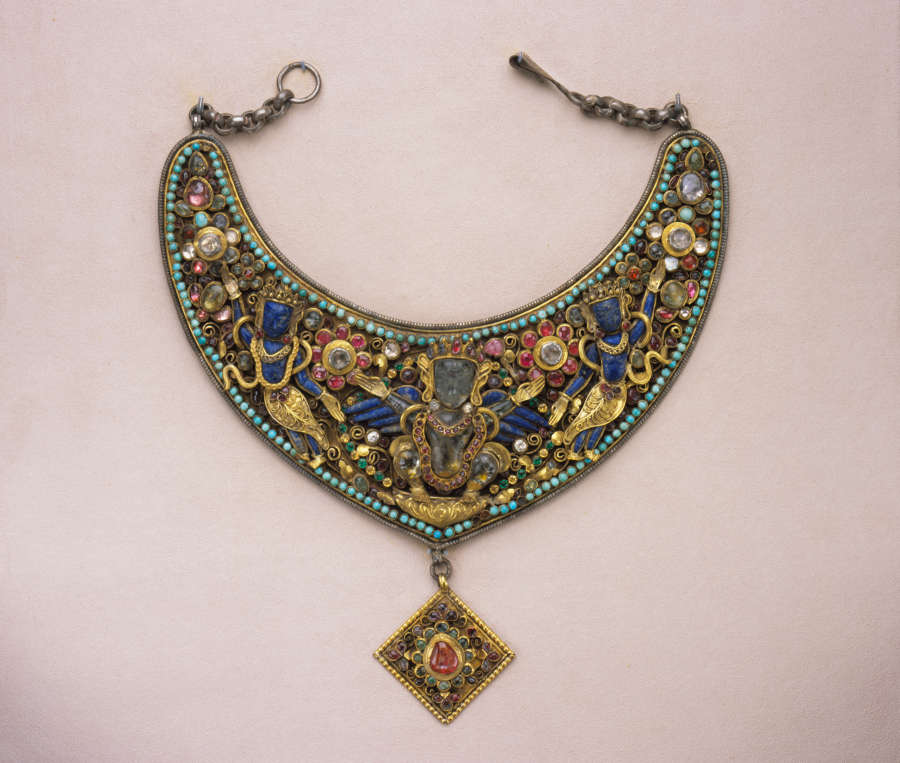 An ornate crescent necklace and gold diamond-shaped pendant, featuring a symmetrical flowing arrangement of green, blue, pink, and golden floral motifs and figures in precious metals, stones and beads.