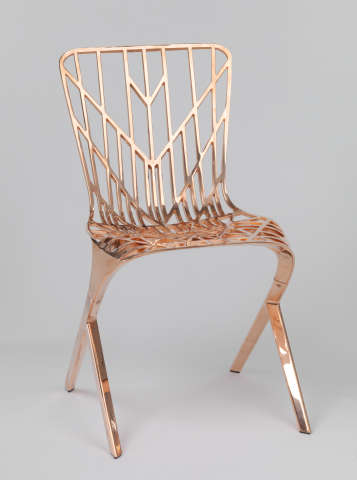 A copper-colored chair with an angular and open frame, with a symmetrical geometric pattern on the seat and backrest.