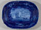 A platter with dark blue decorations depicting a coastal scene. Images of shells along the border.
