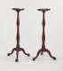 A pair of tall, wooden candle stands with turned legs and ornate, tripod feet.