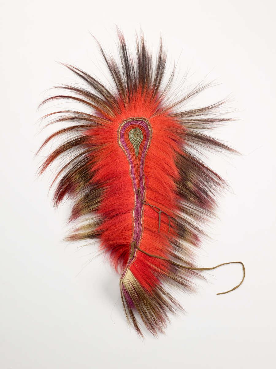 Back of a tear-drop shaped headdress with a red and green interior from which long black, red, and pink gradient feathers emerge with a string at the end.