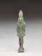 Standing light-jade and brown sculpture of a standing person with a tall head, narrow torso, and straight arms. The left leg has brown specks on it while the headdress is light and translucent.