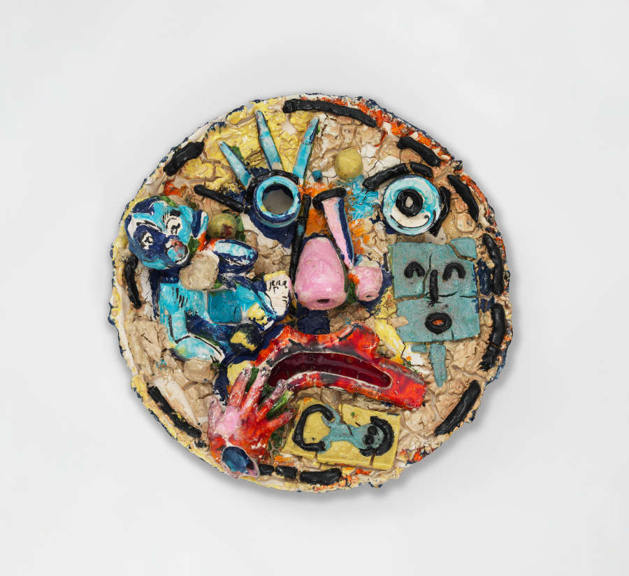 Ceramic disk with a cracked colorful surface showing a fragmentary frowning face with features made up of disjointed shapes and various symbols such as a blue baby and a red hand.