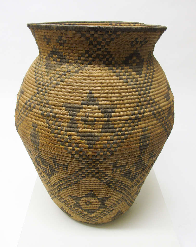 Round woven tan jar with a narrow base and bulging body with a flared neck. The jar features dark brown diagonally intersecting lines with 6-pointed stars in each square. 