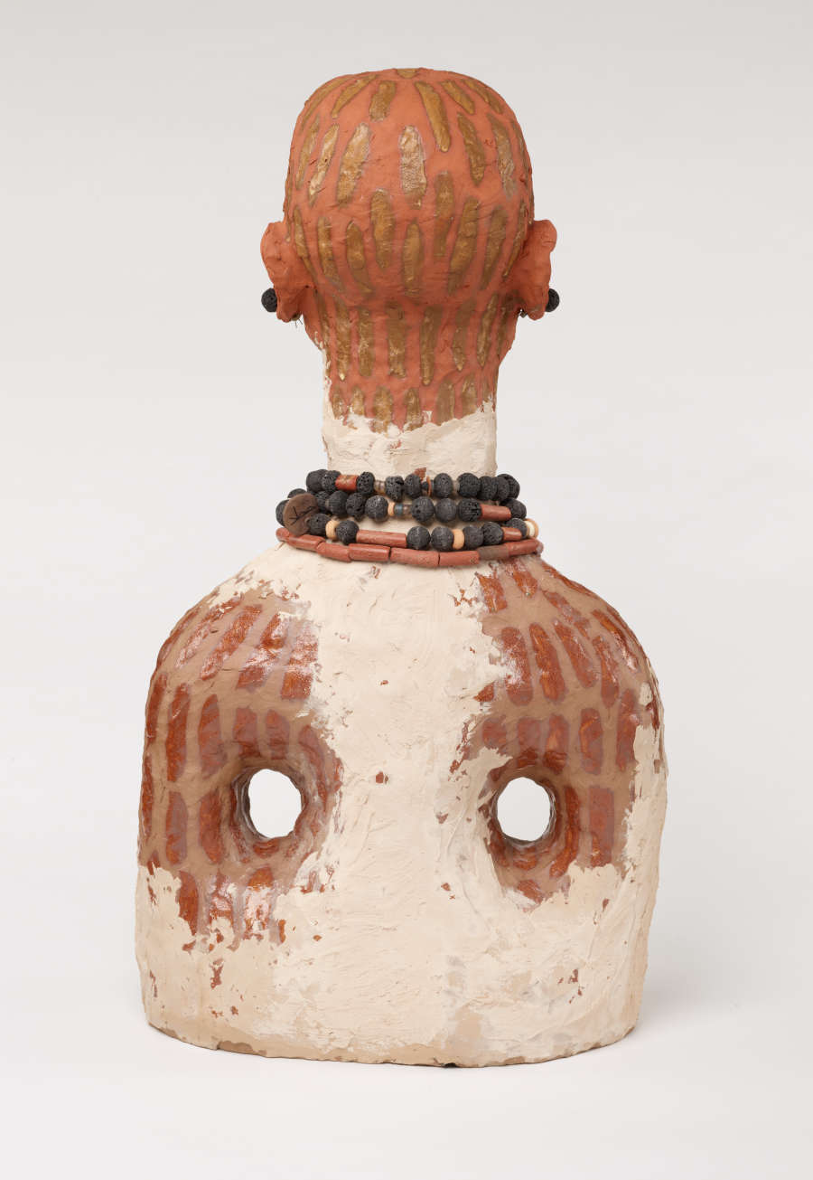 Back view of the bust. The painted brown patterns overlap with the two holes in the torso. The white paint on her back travels up to the spine to the middle of their neck. 