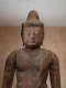 Close up of a weathered wooden Buddha statue with a serene expression and a robe draped over the right shoulder.