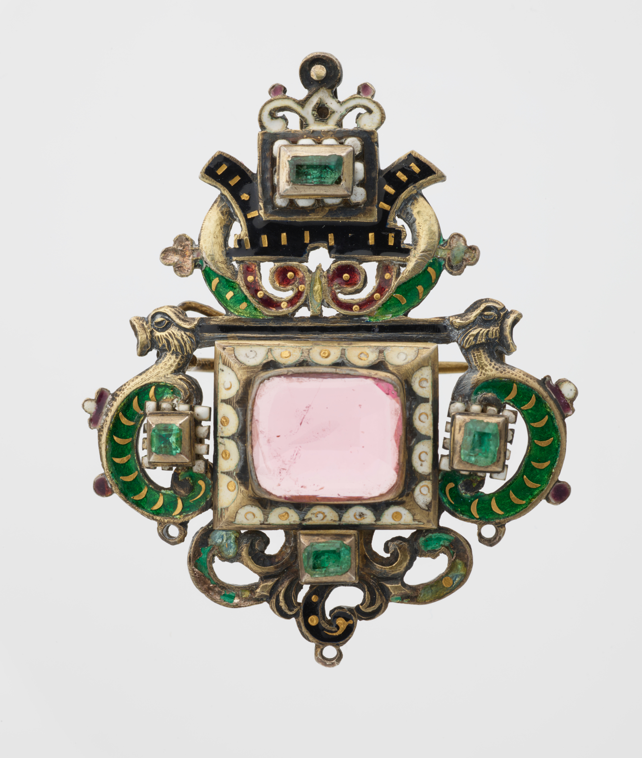 An ornate brooch featuring a central pink gemstone surrounded by enameled decoration in green and black. Two symmetrical dragon heads adorn the sides.