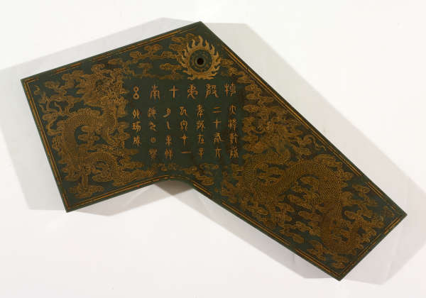 Dark green slab which slopes sharply down to the right, with a dark circle at the top. Features intricate golden embellishments depicting Chinese characters surrounded by dragons above clouds.