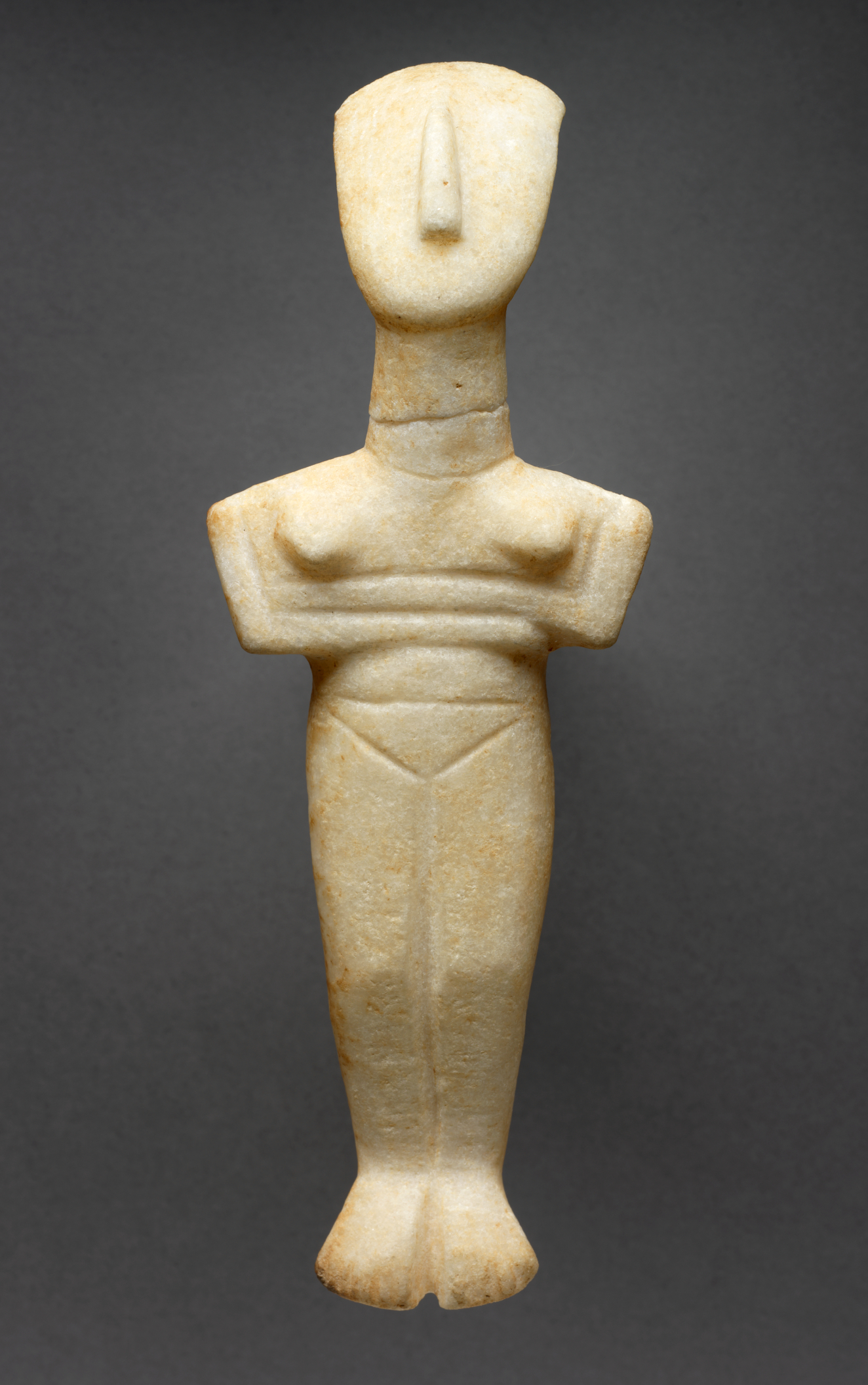 A smooth, cream-colored figurine with a minimalist human form, featuring broad shoulders, narrow waist, and a strong, triangular nose. 
