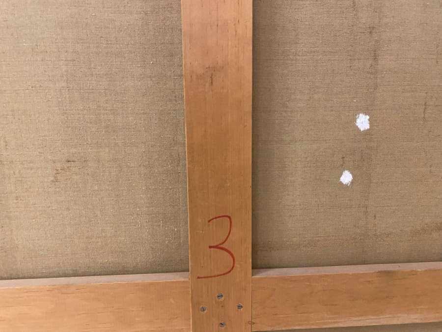 Back of a canvas with a wooden crossbar marked with a large red “3,” beside two white patched spots on the fabric.