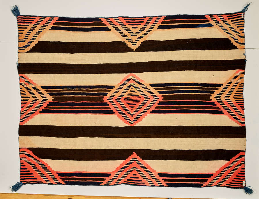 A tasseled, striped woven blanket with three columns and rows of concentric diamonds overtop. The stripes are black and cream of varying widths.