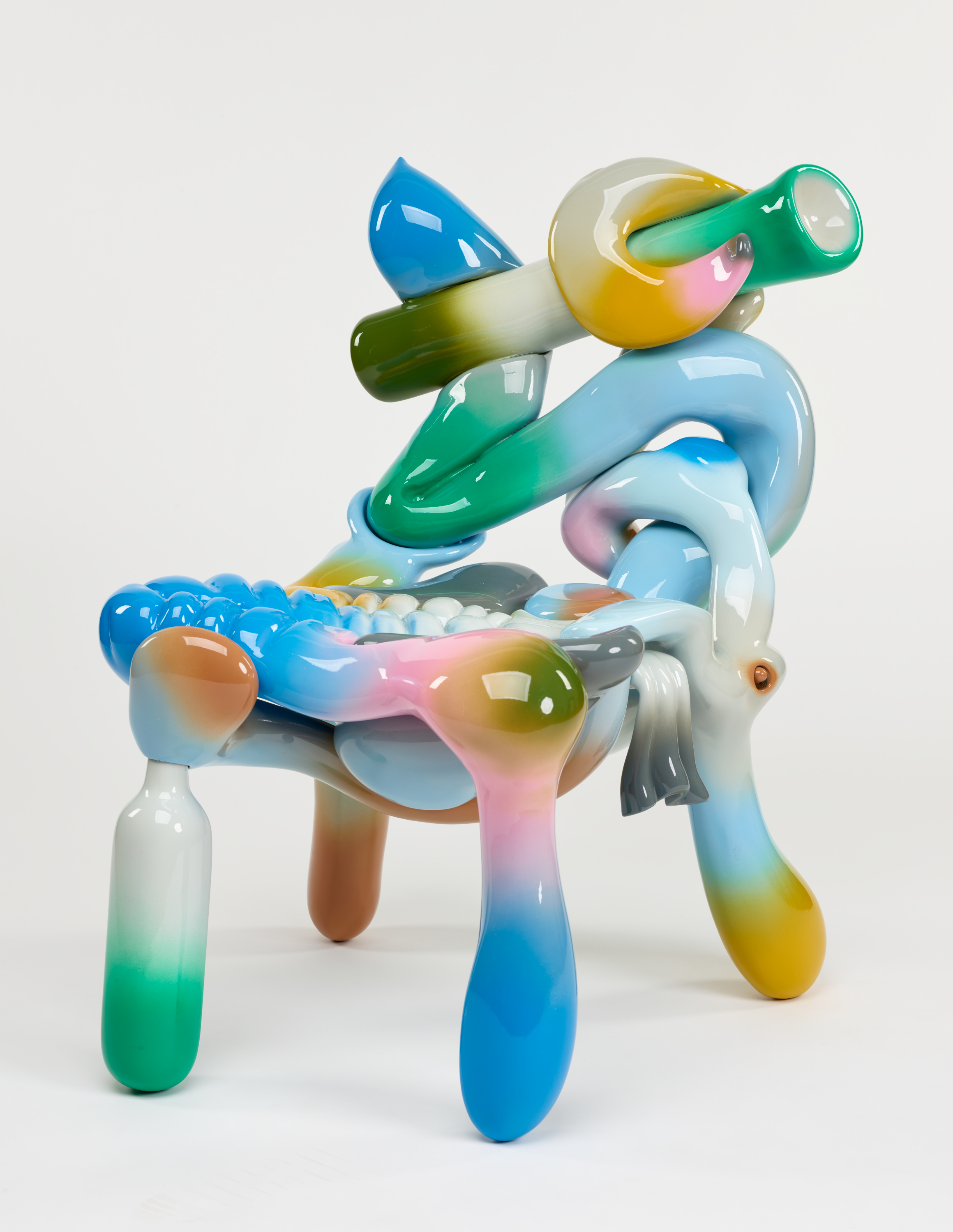 Sculptural chair with intertwined glossy colorful balloon-like shapes arranged in an abstract manner against a stark white backdrop.