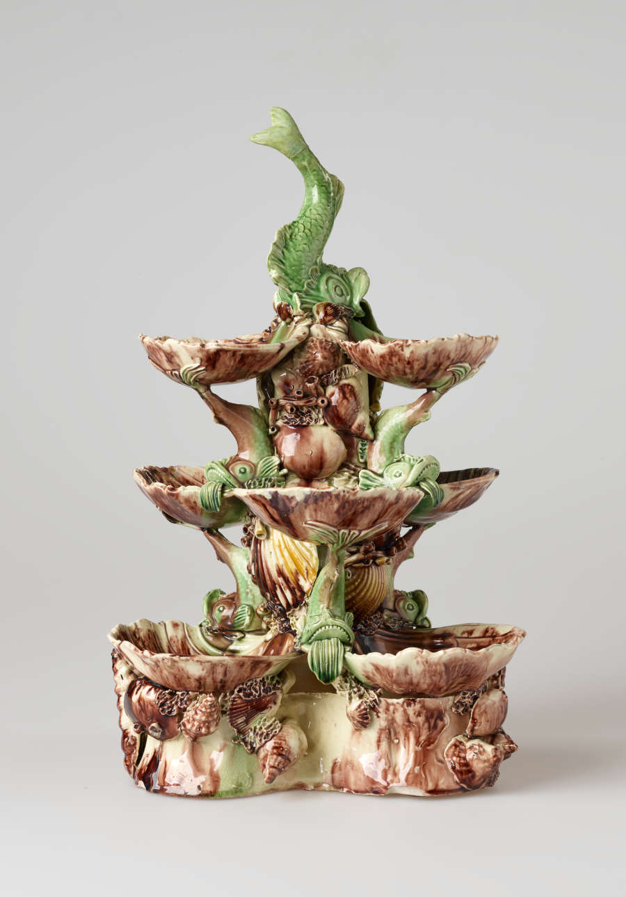 An elaborate, sculptural, three-tiered dish. Colored in brown, green, and cream with floral decorations as well as sculpted fish decorations.